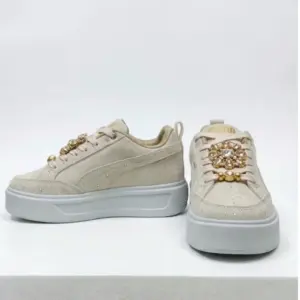 Zapatillas Puma de plataforma en carnaza color beige claro con pedrería y perlas decorativas, vista lateral y frontal.
